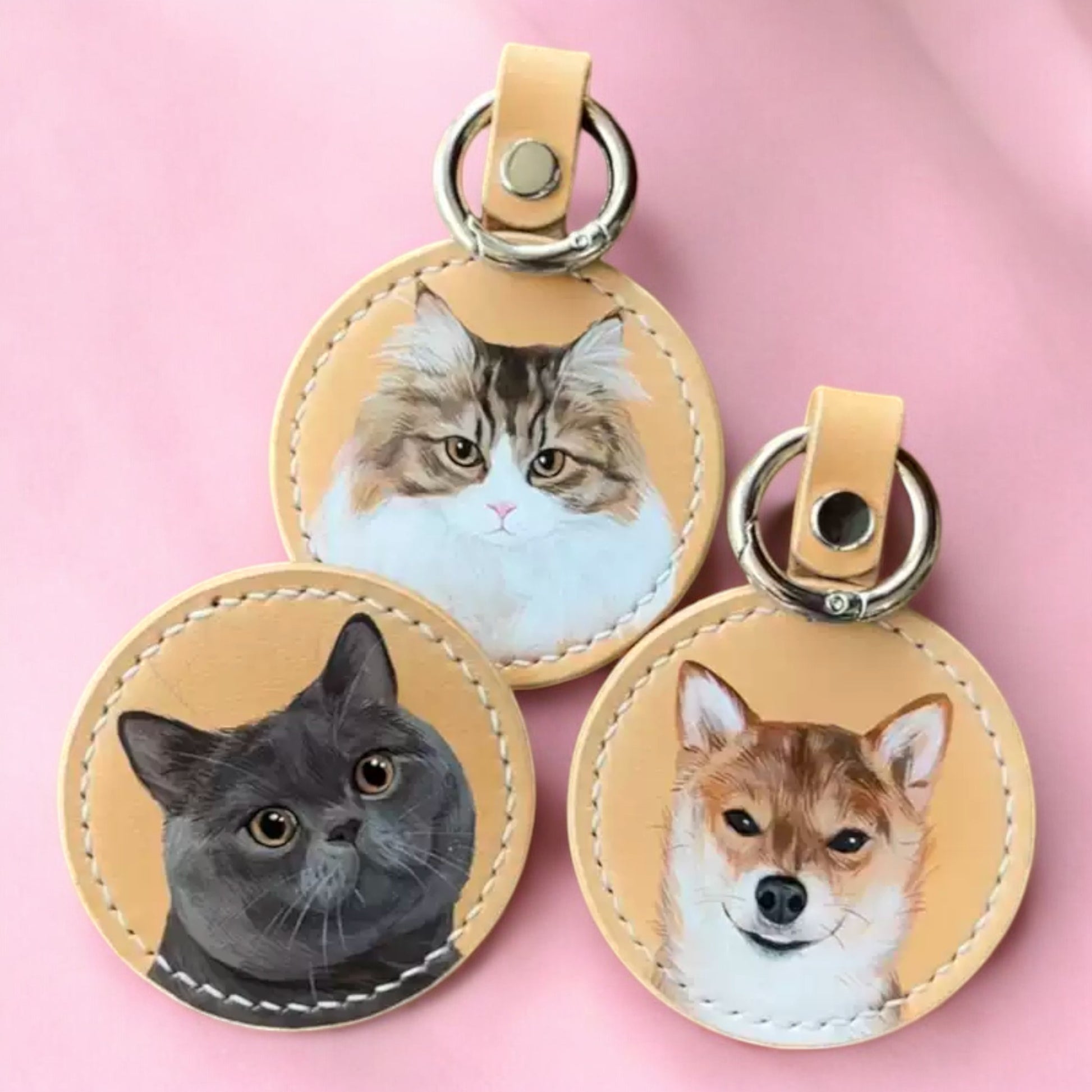 Three personalized leather keychains featuring hand-painted portraits of a Shiba Inu, a Maine Coon, and a British Shorthair, perfect for pet lovers.