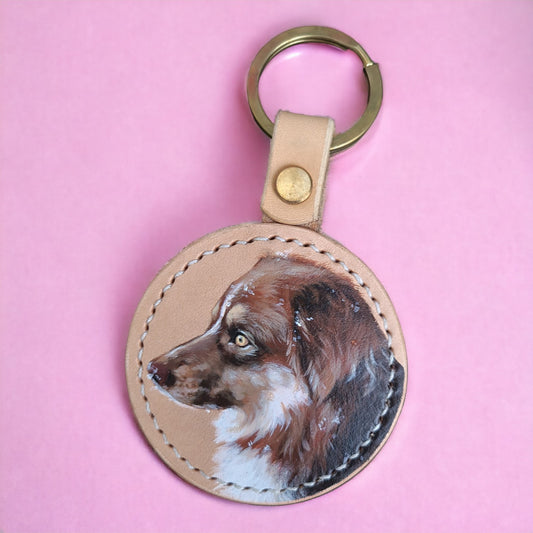 Customizable leather keyring featuring a hand-painted pet portrait of a brown and white colored dog, set against a pink background.