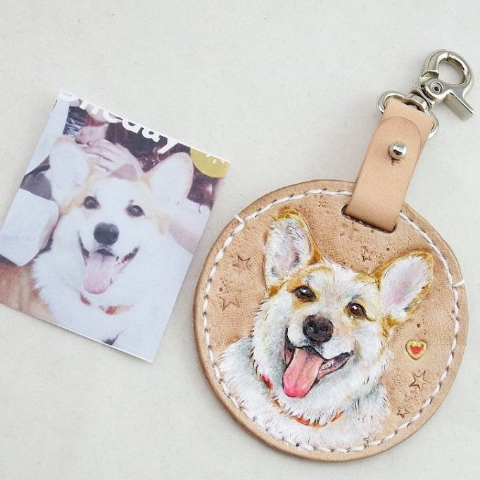 Custom hand-painted leather keychain with a portrait of a white and brown dog, shown with the original photo