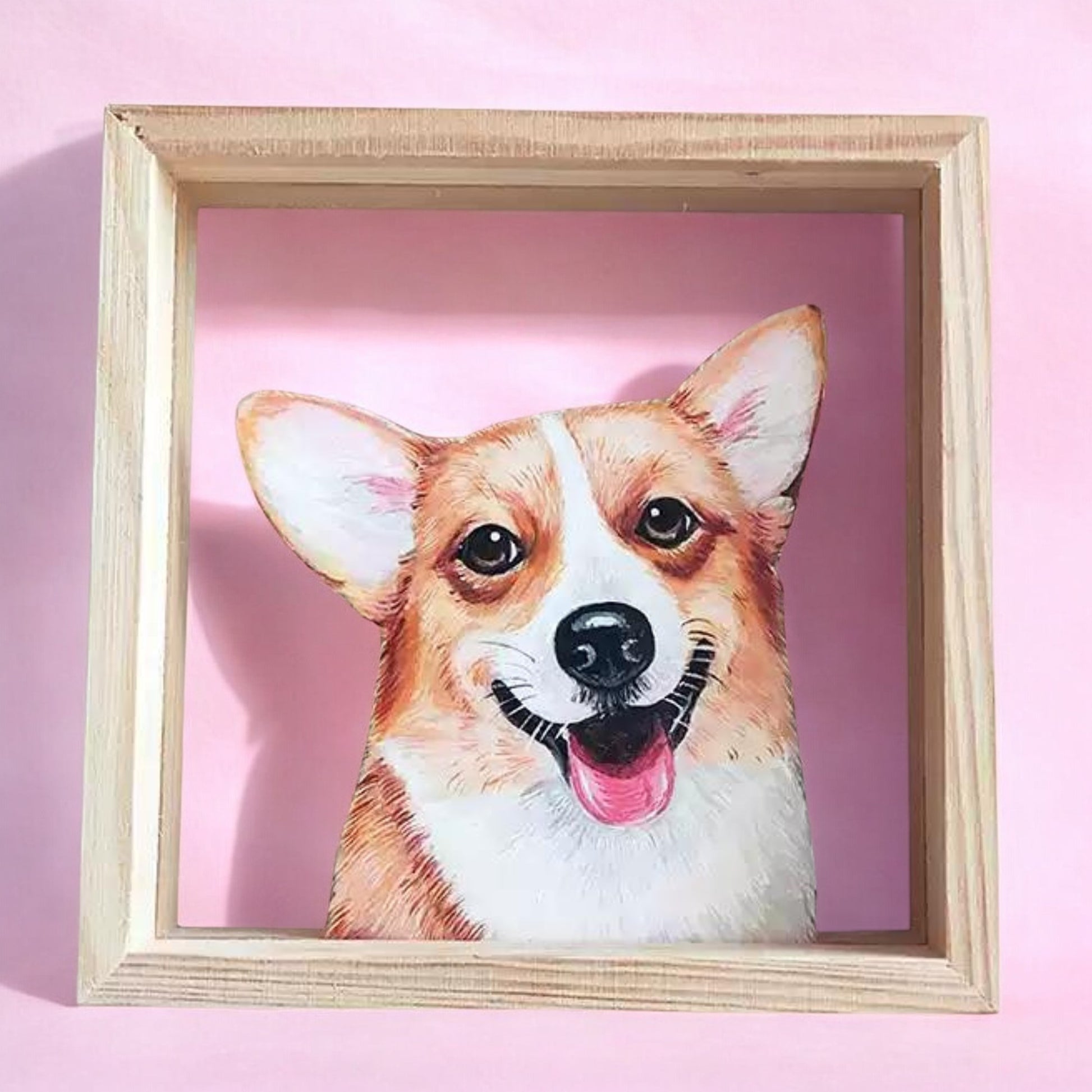 Hand-painted portrait of a happy Corgi dog in a wooden frame, with a light pink background. The artwork captures the Corgi’s joyful expression, showcasing detailed brushstrokes and vibrant colors, perfect for dog lovers and pet portrait enthusiasts.