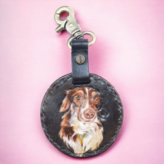 Custom hand-painted leather keychain with a portrait of a brown and white dog, on a pink background