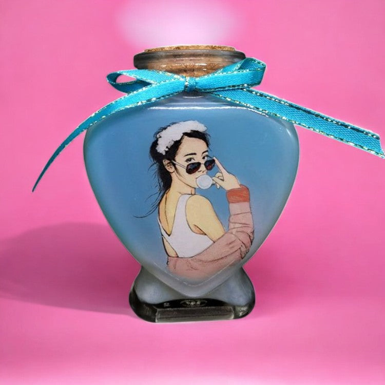 A custom hand-painted portrait of a stylish woman with sunglasses inside a heart-shaped sand bottle, tied with a blue ribbon.