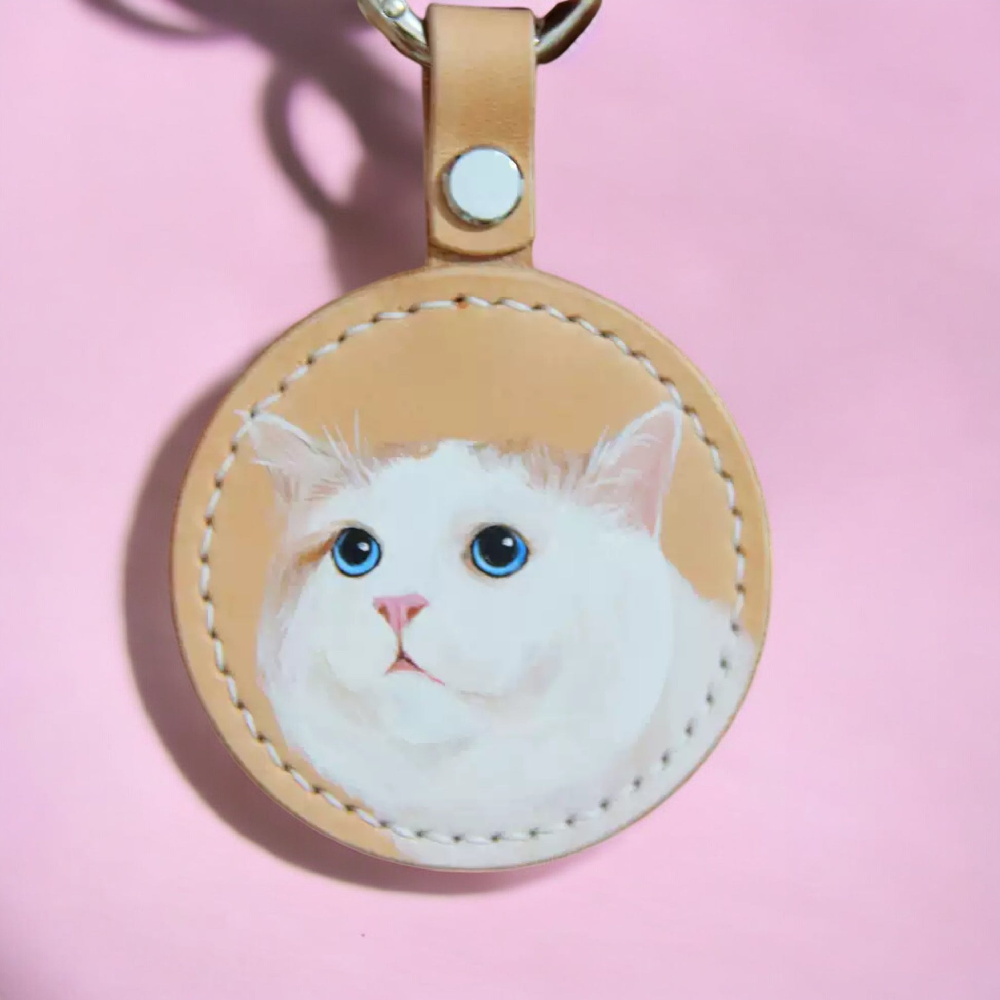 Custom hand-painted white cat portrait on a leather keychain, highlighting soft fur textures and vivid blue eyes.