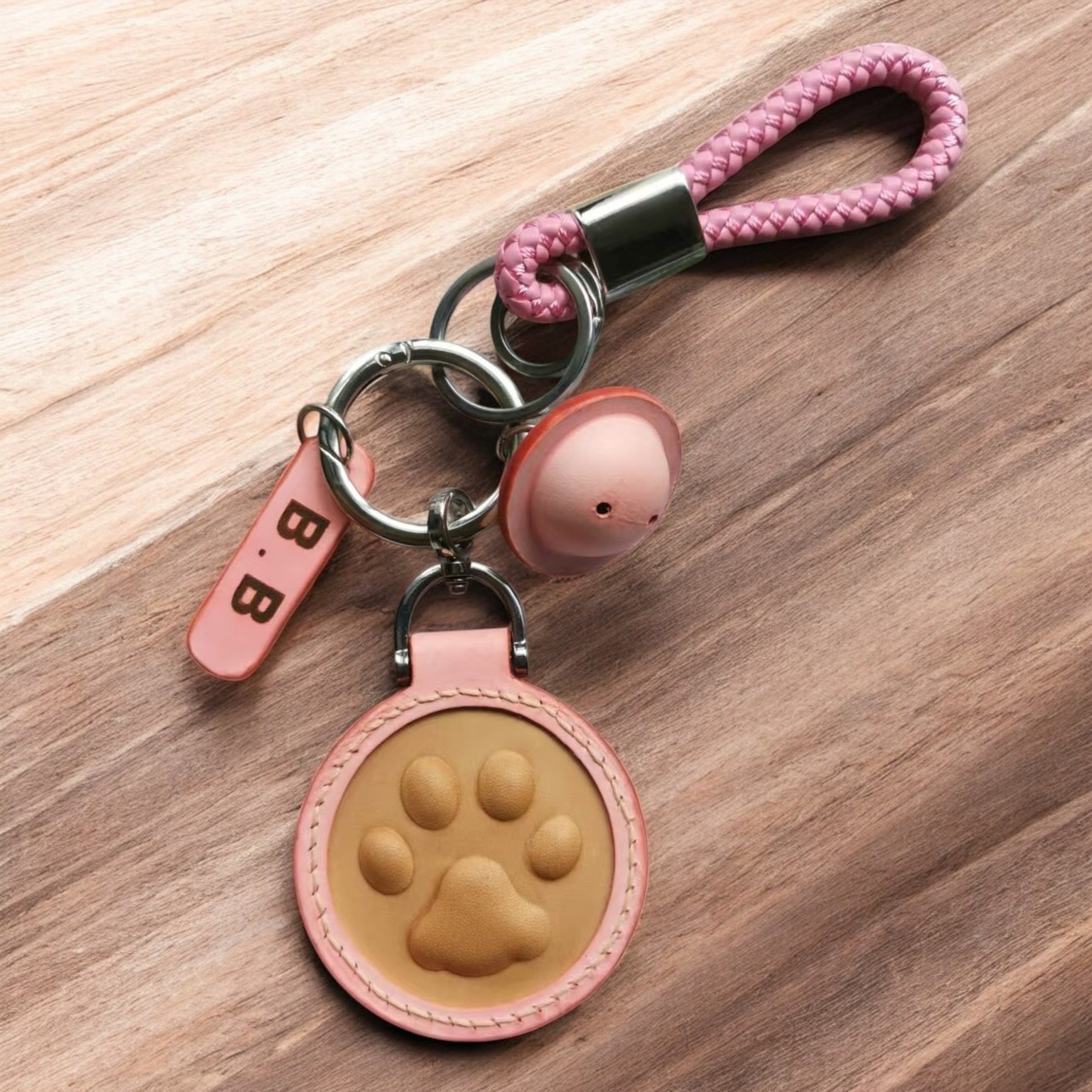 A pink leather keychain with a embossed pawprint, braided loop, metal keyring and a tag on a wooden background.