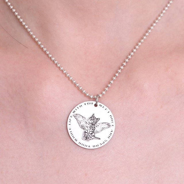 Sterling silver pendant necklace with a cat's face and wings, worn on a neck.