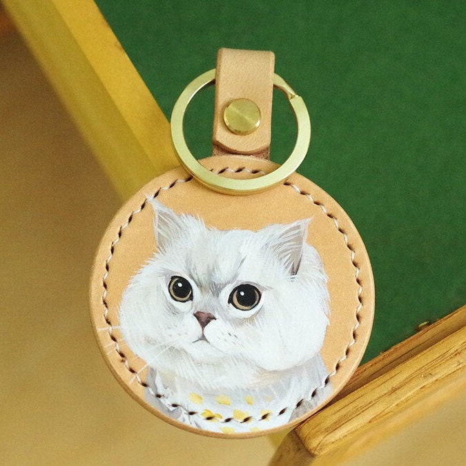 Handpainted leather keychain with a portrait of a white cat with green eyes.