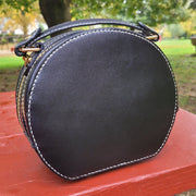 Back view of a round leather handbag with custom pet portrait painting