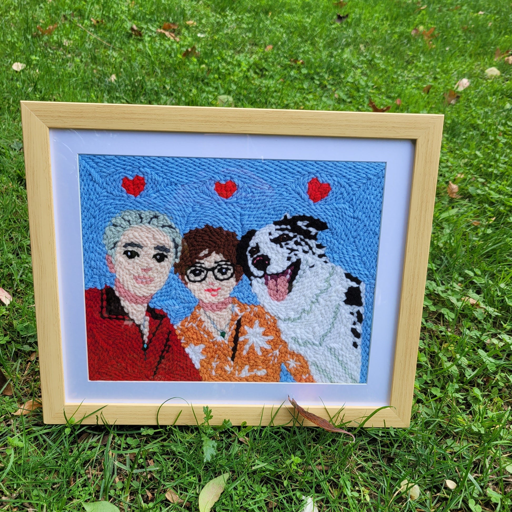 Framed custom needle punch pet portrait displayed outdoors, showing vibrant colors and detailed embroidery.